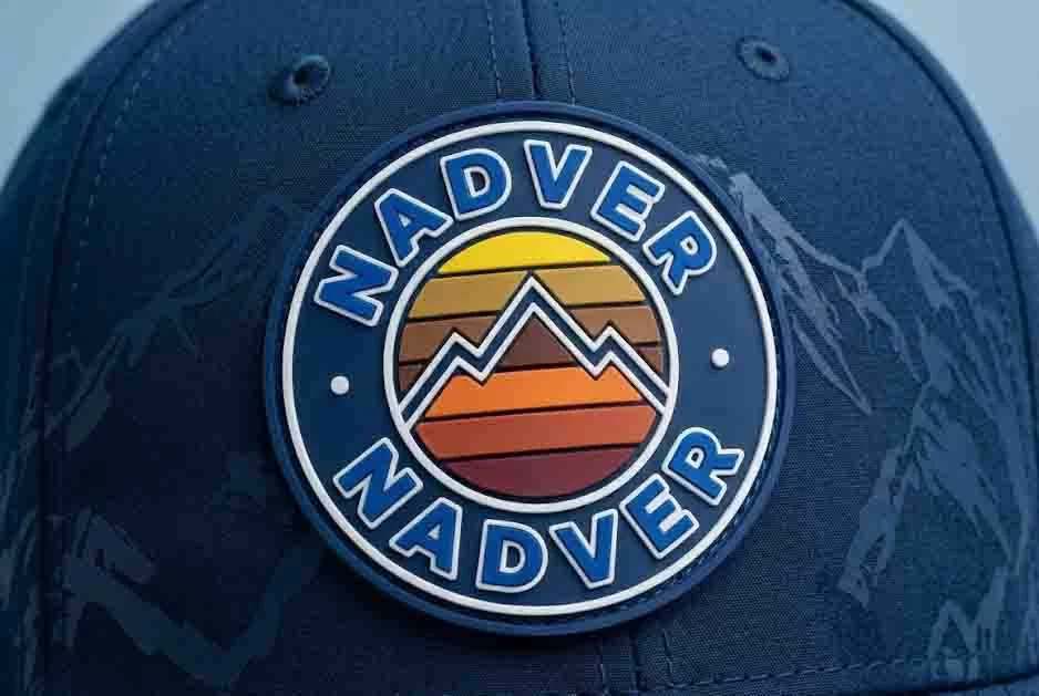 Macro photograph focused on the complex mixed-media decoration of a black premium baseball cap, combining a central woven patch with bold, thick scarlet 3D puff embroidery and tone-on-tone screen print.